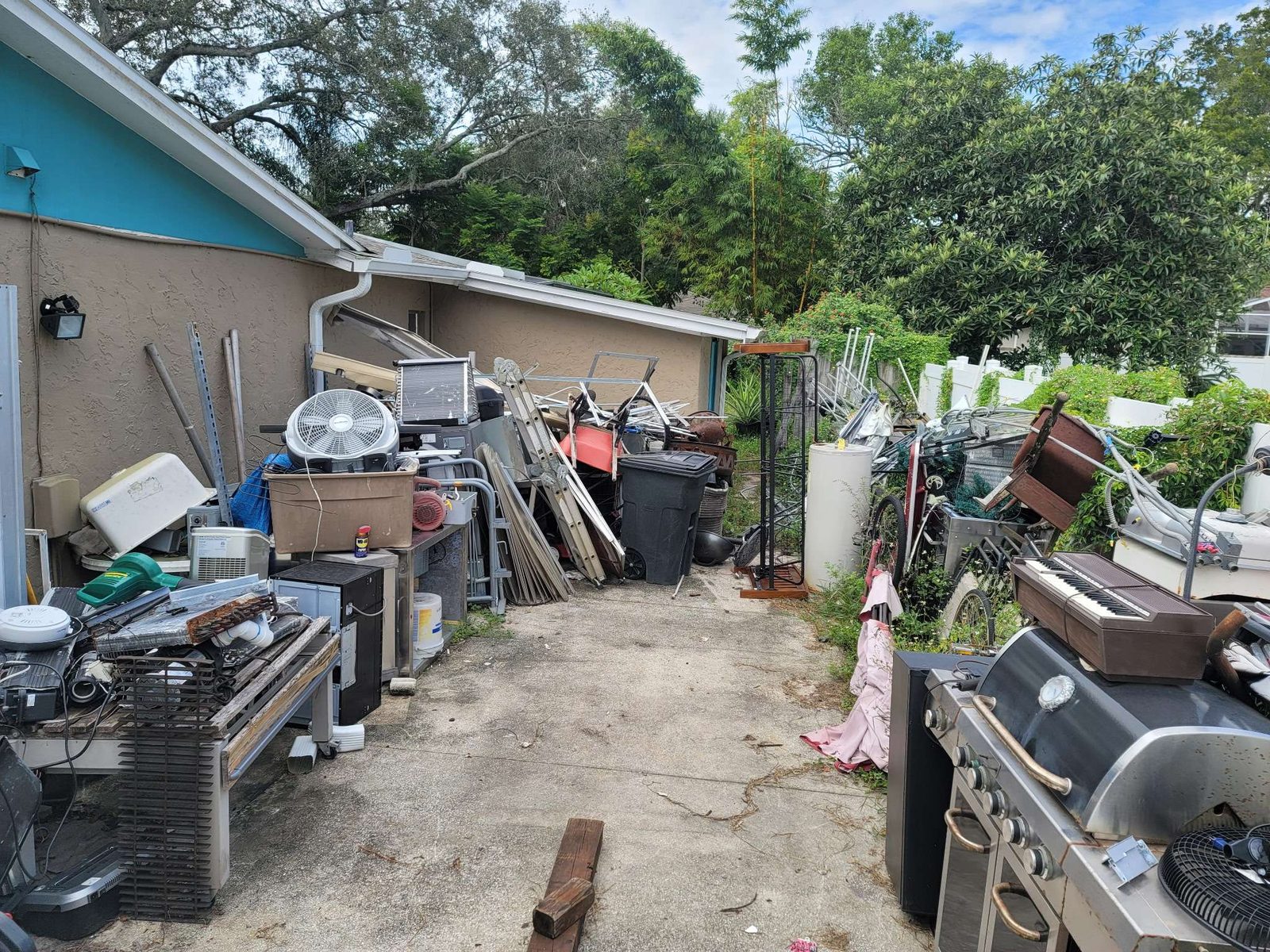 Before: packed side yard with appliances, AC units, and debris piled along house exterior